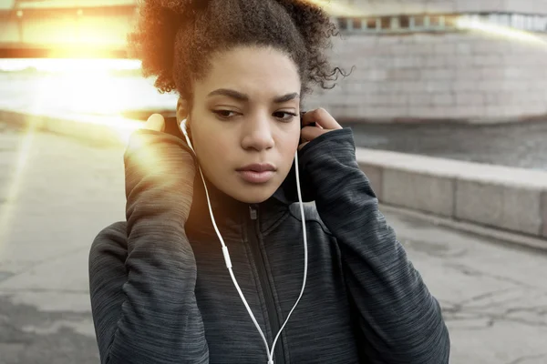 Young sporty African American woman in urban environment preparing for workout at sunset