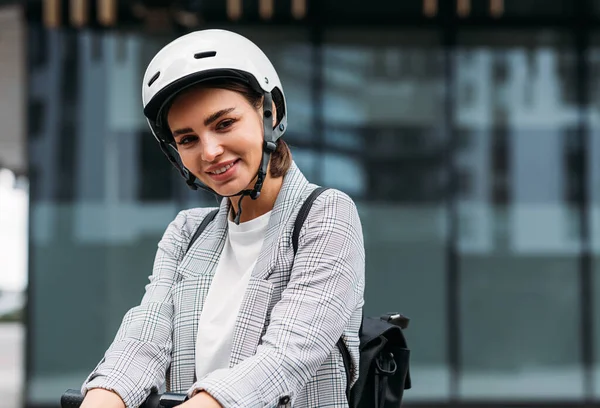 Beautiful smiling businesswoman in cycling helmet lean on handlebar of electric scooter looking at camera