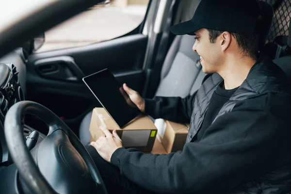 Close up of male courier sitting on a driver\'s seat checking delivery information on a digital tablet