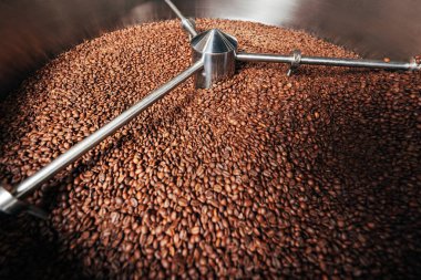 Kahve çekirdekleri ile dolu bir varili soğutma makinesine yakın plan, endüstriyel üretim sürecini gösteriyor.