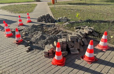 Şehir caddesinde kaldırım onarımı, kazılmış kaldırım taşları trafik güvenliği konileriyle işaretlenmiş.