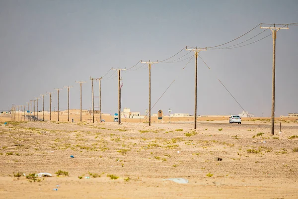 Middle East, Arabian Peninsula, Oman, Al Batinah South, Mahout. A power line and road in the desert of Oman.