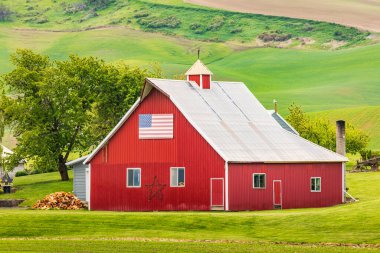 Garfield, Washington, ABD. 24 Mayıs 2021. Palouse tepelerinde Amerikan bayrağı olan kırmızı bir ahır..