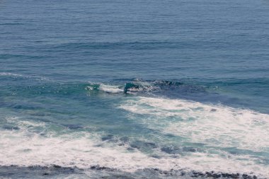 Yüksek açılı turkuaz dalgaların Iquique, Şili 'deki kayalık bir resifin üzerinde beyaz köpüğe dönüşmesi hareketi ve dokusunu gösteriyor.