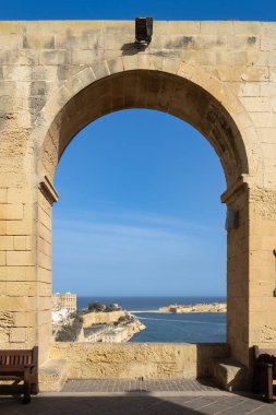 Mavi denizi ve Valletta 'nın tarihi kuvvetlerini berrak bir gökyüzü altında sergilemek için kireçtaşı kemeri kullanan merkezi bir mimari çerçeve.