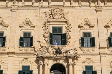 Valletta, Malta 'daki büyük bir kireçtaşı sarayının ön cephesinde süslü barok taş oymalar ve yeşil kepenkler.