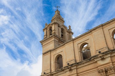 Malta 'da ince bulutlu dramatik mavi gökyüzüne karşı tarihi kireçtaşı kilise çan kulesinin alçak açılı görüntüsü