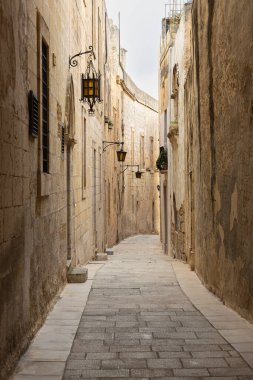 Malta 'nın tarihi kenti Mdina' da fenerlerin asılı olduğu dar, dolambaçlı bir kireçtaşı geçidinin perspektif görüntüsü