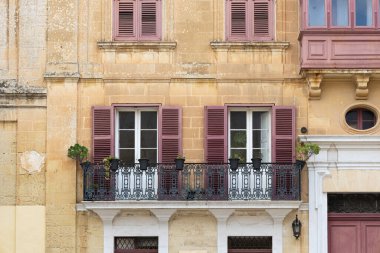 Dekoratif işlenmiş demir balkonu ve Malta 'da geleneksel mor ahşap panjurları olan kireçtaşı bir evin önü.