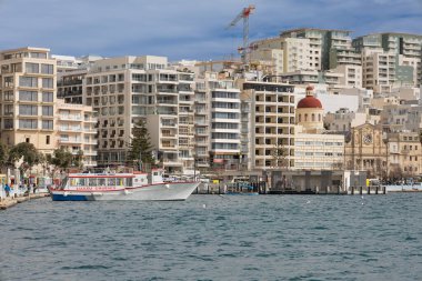 Sliema, Malta - 5 Şubat 2026: Sliema feribot terminaline yanaşan bir gezi teknesi şehrin arka planında ufuk çizgisi olan