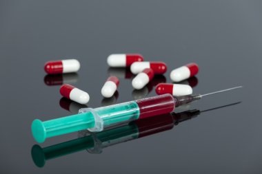 Blood filled hypodermic needle with loose drug capsules on desk