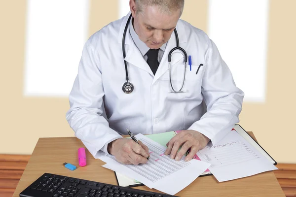 Doctor con estetoscopio alrededor de su cuello en su escritorio escritura —  Fotos de Stock