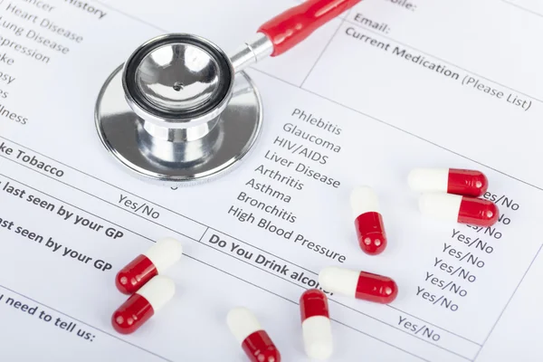 Красный стетоскоп и капсулы с таблетками, лежащие на медицинской форме — стоковое фото