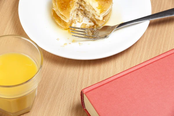 Parte comido panqueques en una mesa de desayuno con un libro — Foto de Stock