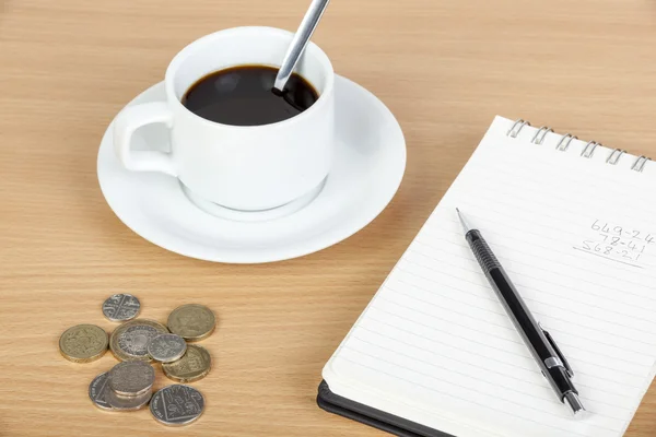 Cup of coffee on table with notepad and coinage — Stock Photo, Image