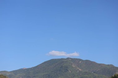 Ufacık bir bulutla kaplı bir dağın tepesindeki engin mavi gökyüzü.