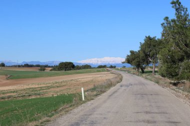 Dağlık kırsal bir arazide asfalt yolu tarımsal alanlarla çevrili.