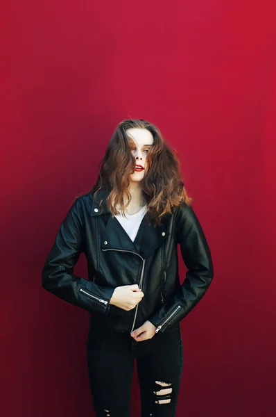 Mujer joven en chaqueta de cuero negro y jeans. Fondo rojo , — Foto de Stock