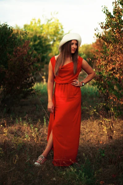 Young beautiful girl in a stunning long red dress and white hat — Stok fotoğraf