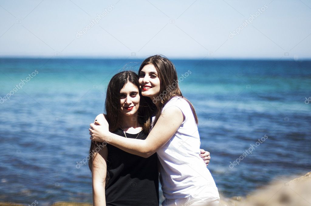 Sisters at beach hugging each other. Portrait of beautiful young