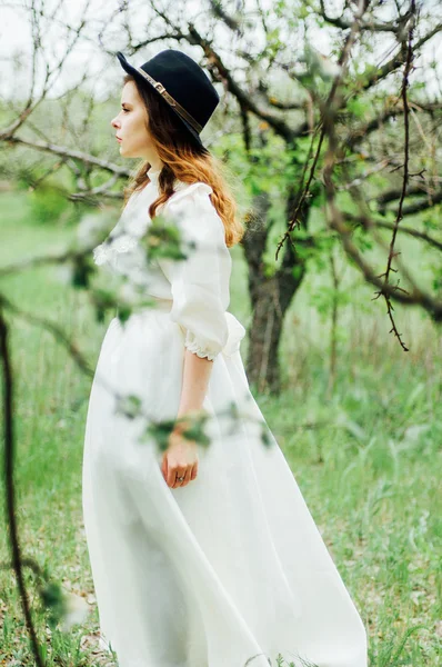 Chica joven en un vestido blanco y sombrero negro en el en el blanco fl — Foto de Stock