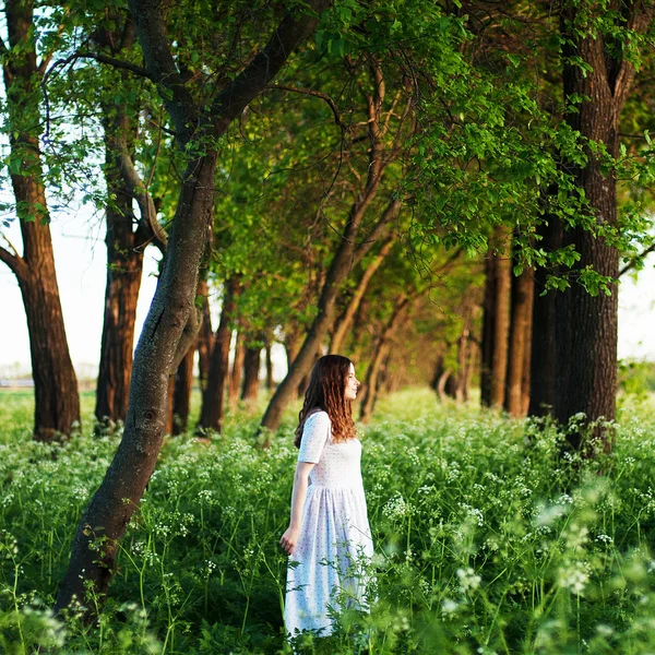 Uzun beyaz elbiseli ve gün batımında tarlada uzun altın kıvırcık saçlı güzel genç bir kadın. Fotoğraf tonda stil Instagram vsco filtreler. Çiçek tarlalarında açık poz genç güzel kadın. — Stok fotoğraf