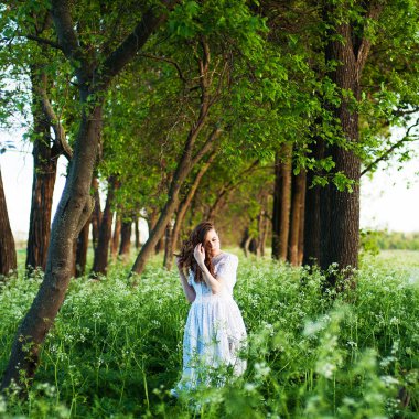 Uzun beyaz elbiseli ve gün batımında tarlada uzun altın kıvırcık saçlı güzel genç bir kadın. Fotoğraf tonda stil Instagram vsco filtreler. Çiçek tarlalarında açık poz genç güzel kadın.