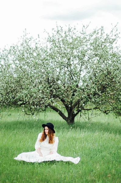 Όμορφη νεαρή γυναίκα με μακρύ λευκό φόρεμα και με μακριά χρυσά σγουρά μαλλιά στο χωράφι το ηλιοβασίλεμα. Φωτογραφία τονισμένο στυλ Instagram VSCO φίλτρα. Νεαρή όμορφη γυναίκα που ποζάρει εξωτερική στα λουλούδια χωράφια. — Φωτογραφία Αρχείου