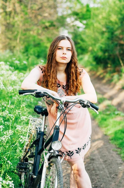 Outdoor fashion portrait of elegant lady standing near hipster bicycle in pink stylish dress. Enjoy and having fun spring day in the park with a vsco filters. Beautiful  girl with long thick wavy hair — Stock Photo, Image