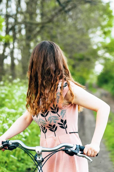 Retrato de moda ao ar livre de senhora elegante em pé perto de bicicleta hipster em vestido rosa elegante. Aproveite e divirta-se dia de primavera no parque com um filtros vsco. Menina bonita com cabelo ondulado grosso longo — Fotografia de Stock