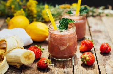 muz ve çilek güler yüzlü. Mutfak masasında malzemelerle bardaklarda iki soğuk çilek muz Smoothies. Çilek Muz Smoothie taze malzemelerle hazırlanan. Taze çilek güler yüzlü