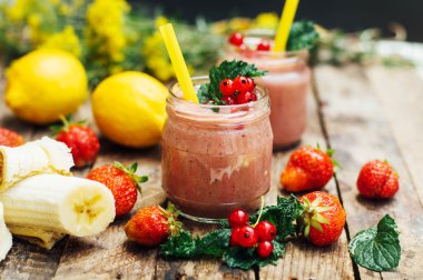 muz ve çilek güler yüzlü. Mutfak masasında malzemelerle bardaklarda iki soğuk çilek muz Smoothies. Çilek Muz Smoothie taze malzemelerle hazırlanan. Taze çilek güler yüzlü