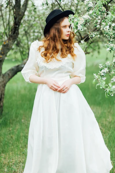 Chica joven en un vestido blanco y sombrero negro en el en el blanco fl — Foto de Stock