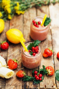 muz ve çilek güler yüzlü. Mutfak masasında malzemelerle bardaklarda iki soğuk çilek muz Smoothies. Çilek Muz Smoothie taze malzemelerle hazırlanan. Taze çilek güler yüzlü