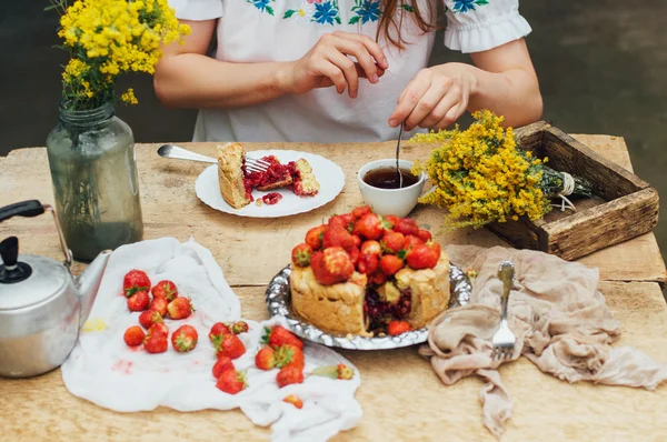 Woman eating a delicious home-made cake with aisheny and stuffed strawberries for dessert. Summer Styled dinner table. Coffee to the cake. sitting at the rustic dining table