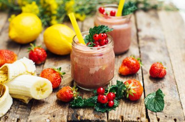 muz ve çilek güler yüzlü. Mutfak masasında malzemelerle bardaklarda iki soğuk çilek muz Smoothies. Çilek Muz Smoothie taze malzemelerle hazırlanan. Taze çilek güler yüzlü