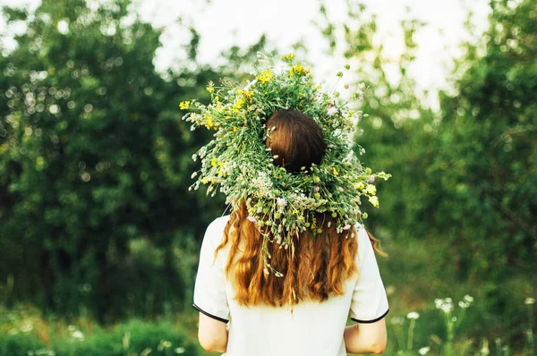 Bella ragazza nella ghirlanda di fiori nel prato nella giornata di sole. Ritratto di Giovane bella donna che indossa una corona di fiori selvatici. Giovane pagana ragazza slava cerimonia di condotta in mezza estate . — Foto Stock