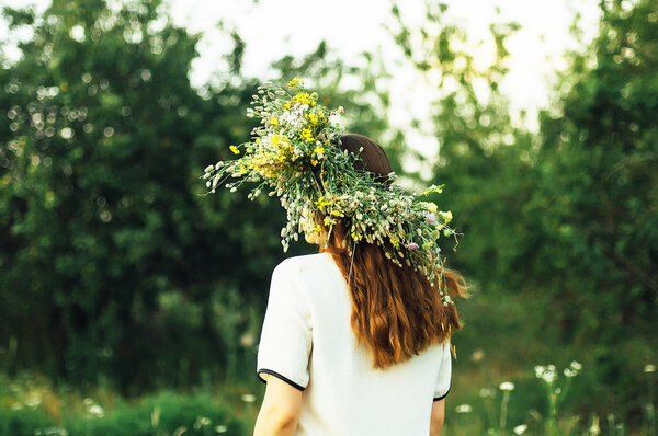 beautiful girl in wreath of flowers  in meadow on sunny day. Portrait of Young beautiful woman wearing a wreath of wild flowers. Young pagan Slavic girl conduct ceremony on Midsummer.
