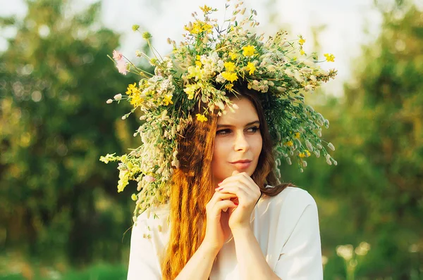 Krásná dívka v věnec z květin na louce na slunečný den. Portrét mladé krásné ženy nosí věnec divokých květů. Mladá pohanské slovanské dívky provádět obřad slunovratu. — Stock fotografie
