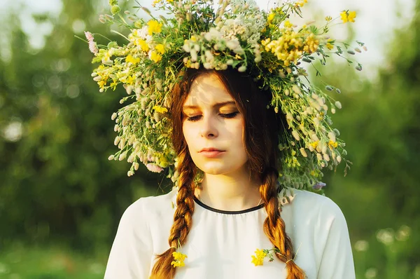 Mooi meisje in een krans van bloemen in de weide op zonnige dag. Portret van jonge mooie vrouw het dragen van een krans van wilde bloemen. Jonge heidense Slavische meisje gedrag ceremonie op Midsummer. — Stockfoto