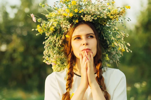 Mooi meisje in een krans van bloemen in de weide op zonnige dag. Portret van jonge mooie vrouw het dragen van een krans van wilde bloemen. Jonge heidense Slavische meisje gedrag ceremonie op Midsummer. — Stockfoto