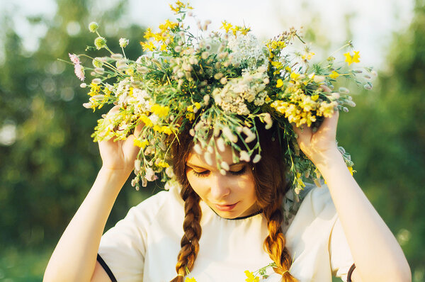 beautiful girl in wreath of flowers  in meadow on sunny day. Portrait of Young beautiful woman wearing a wreath of wild flowers. Young pagan Slavic girl conduct ceremony on Midsummer.