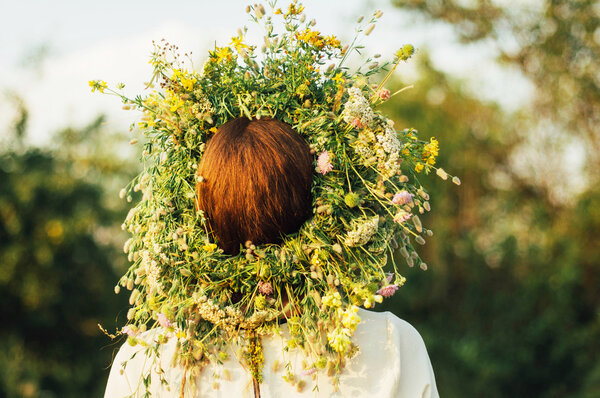 beautiful girl in wreath of flowers  in meadow on sunny day. Portrait of Young beautiful woman wearing a wreath of wild flowers. Young pagan Slavic girl conduct ceremony on Midsummer.
