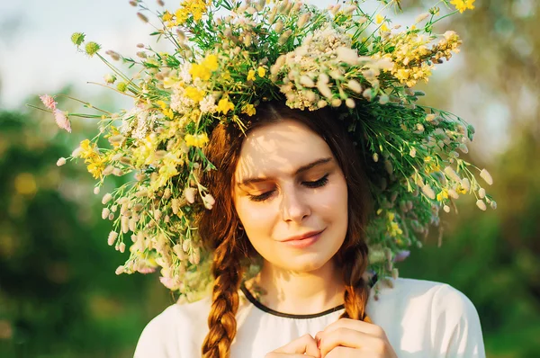 Schönes Mädchen im Blumenkranz auf der Wiese an einem sonnigen Tag. Porträt einer jungen schönen Frau mit einem Kranz aus wilden Blumen. junges heidnisches slawisches Mädchen führt Zeremonie im Hochsommer durch. — Stockfoto