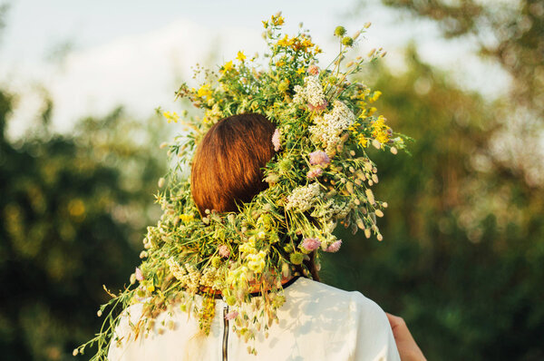 beautiful girl in wreath of flowers  in meadow on sunny day. Portrait of Young beautiful woman wearing a wreath of wild flowers. Young pagan Slavic girl conduct ceremony on Midsummer.