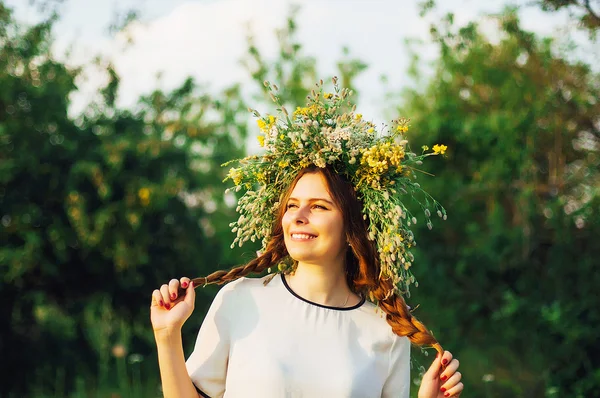 Mooi meisje in een krans van bloemen in de weide op zonnige dag. Portret van jonge mooie vrouw het dragen van een krans van wilde bloemen. Jonge heidense Slavische meisje gedrag ceremonie op Midsummer. — Stockfoto