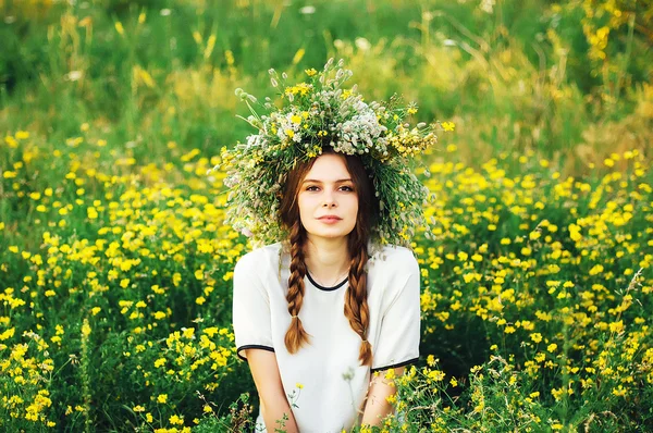 Menina bonita na grinalda de flores no prado no dia ensolarado. Retrato de jovem mulher bonita vestindo uma coroa de flores silvestres. Jovem pagão eslavo menina cerimônia de conduta no verão . — Fotografia de Stock