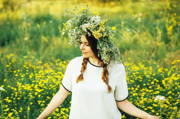 Beautiful girl in wreath of flowers  in meadow on sunny day. Portrait of Young beautiful woman wearing a wreath of wild flowers. Young pagan Slavic girl conduct ceremony on Midsummer. — Stock Photo, Image