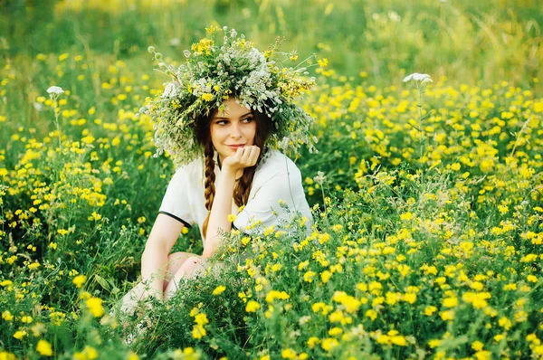 Vacker flicka i krans av blommor i ängen på solig dag. Porträtt av ung vacker kvinna som bär en krans av vilda blommor. Unga pagan slavisk flicka utföra ceremonin på midsommar. — Stockfoto