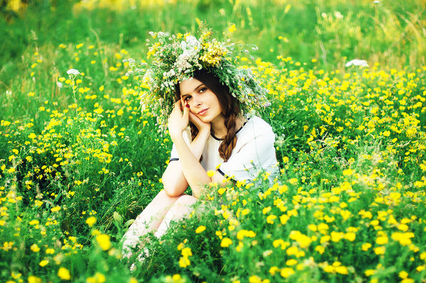 beautiful girl in wreath of flowers  in meadow on sunny day. Portrait of Young beautiful woman wearing a wreath of wild flowers. Young pagan Slavic girl conduct ceremony on Midsummer.